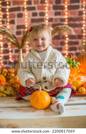 little girl in white warm knitted sweaters in an interior decorated with blankets and pillows as well as pumpkins, autumn leaves and apples. Autumn mood. halloween