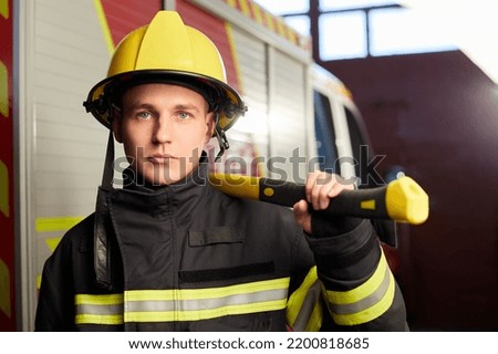 Firefighter fully equipped with helmet and ax in fire truck background. 