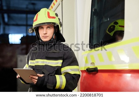 Male firefighter with tablet in uniform on car background