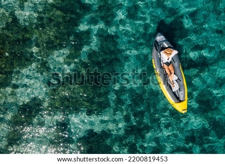 A lonely female in a straw hat relaxing lying in floating inflatable kayak on the turquoise Adriatic Sea waves. Aerial coastal top view shot. Exotic countries vacations concept. Royalty-Free Stock Photo #2200819453