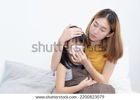 Asian Mother Placing her hand to forehead and wiping her sick daughter nose with tissue Royalty-Free Stock Photo #2200823079