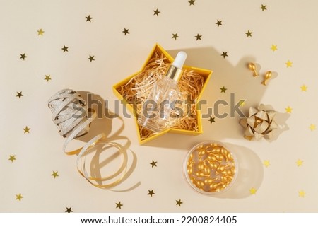 A face antiaging serum or essential oil in golden capsules as a present for Christmas holidays lying in a gift box on a beige background with bright yellow confetti stars around it