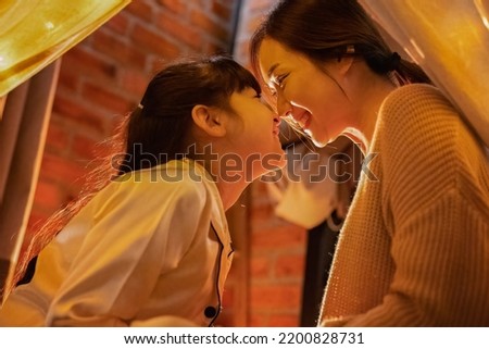 At home in night time mother play and read storytelling book to her daughter and watch excite movie from computer tablet pc until kid fall sleep 
