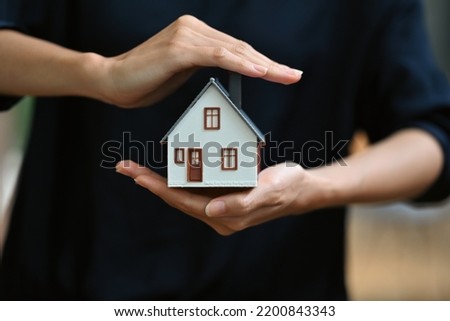 Protect your house concept. Small model of house covered by hands. Royalty-Free Stock Photo #2200843343