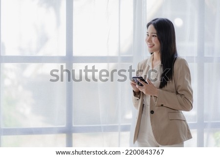Successful young Asian businesswoman smirking at her desk in the office vertical picture