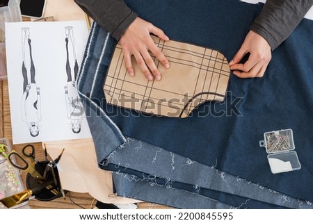 Top view of african american craftswoman holding sewing print near denim cloth and sketch in workshop