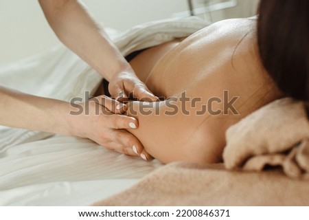 Closeup photo of young woman with bare back getting shoulder massage by professional masseur
