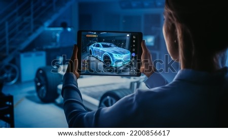 Automotive Engineer Working on Electric Car Chassis Platform, Using Tablet with Augmented Reality 3D Software. Innovative Facility Concept: Vehicle Frame with Wheels Becomes a VFX Virtual Model. Royalty-Free Stock Photo #2200856617