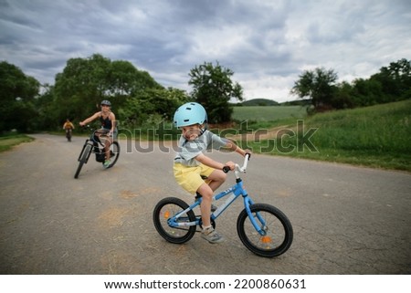 Portrait of excited little boy with his family at backround riding bike on path in park in summer