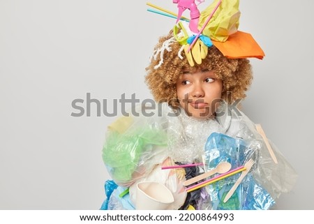 Ecology and volunteering concept. Puzzled confused woman poses in litter costume purses lips looks aside has displeased expression stands indoor against grey background mock up space for text