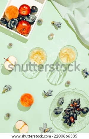 Creative composition made of plate with fruits, glasses, apples and peach on pastel green sunlit background with shadows. Summer and refreshment concept. Harvest theme. Top view. Flat lay