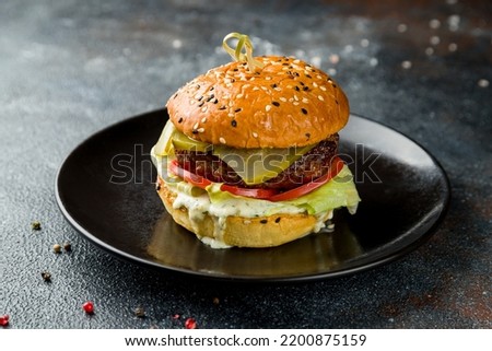 Burger with meat patty, vegetables and salted cucumbers on dark plate