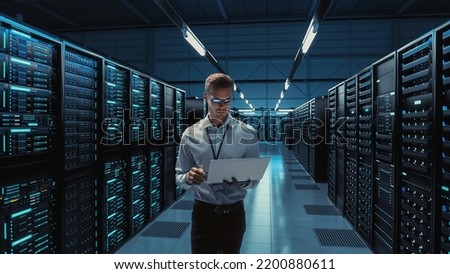 Futuristic Concept: Big Data Center Chief Technology Officer Using Laptop Standing In Warehouse, Information Digitalization Lines Streaming Through Servers. SAAS, Cloud Computing, Web Service Royalty-Free Stock Photo #2200880611