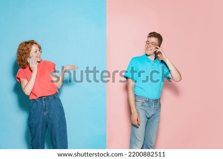 Portrait of young couple, cheerfully talking on phone isolated over pink blue studio background. Excited news spreading. Concept of youth, emotions, facial expression, love, relationship. Poster, ad