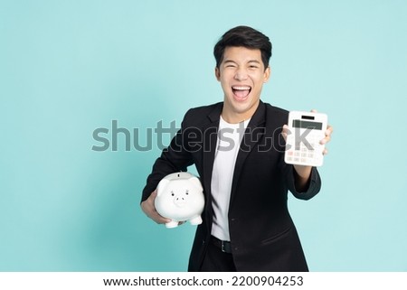 Portrait of Happy Asian businessman holding white piggy bank and calculator isolated on green background, Saving money and financial economize concept Royalty-Free Stock Photo #2200904253
