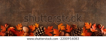 Colorful fall leaves, nuts and pine cones. Bottom border over a rustic dark banner background. Top view with copy space. Royalty-Free Stock Photo #2200916083