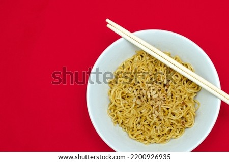 copy space flat lay of tasty fried noodle or indomie goreng served on white bowl with chop stick isolated on red background. fried instant noodle.