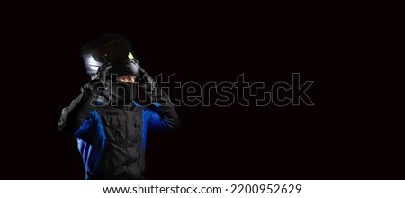 male motorcyclist in a motorcycle outfit and a balaclava puts on a helmet on a dark background. The concept of protective equipment for a biker. Royalty-Free Stock Photo #2200952629