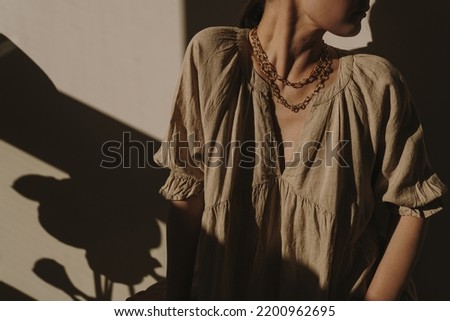 Young pretty woman in linen dress and against the wall. Silhouette in sunlight. Shadows on the wall. Minimal fashion design concept. Aesthetic