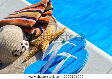 Flip flops, a large starfish, a panama hat and a colorful towel next to the pool. Summer holiday concept on the background of blue water.