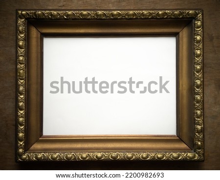 Antique gold frame on a wooden background with a white middle. Vintage gold-colored picture frame.