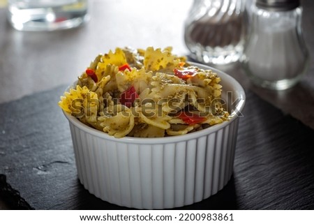 Farfalle pasta with pesto sauce and pieces of red hot pepper in a white bowl