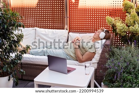 Adult senior plus size woman having online hypnotherapy session with psychotherapist lying on sofa on outdoor terrace at home. 
