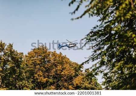 A military stealth helicopter flies low near green trees against a blue sky. Photo of the vehicle.