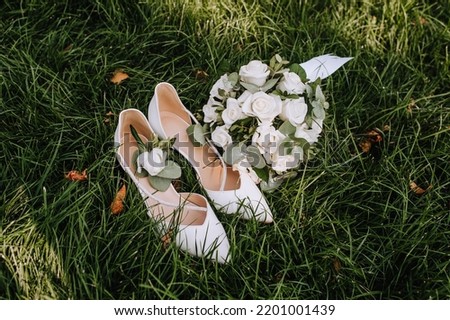 A bride's bouquet of white roses and women's leather shoes stand on green grass close-up. Wedding photography, top view, idea, composition.