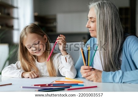 Happy caucasian little girl with elderly grandma with colorful pencils draw picture on table, enjoy study and free time in living room interior. Love and relationships at home ,study and art together