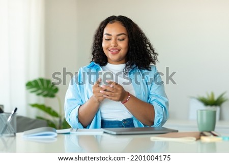 Happy African American Business Woman Using Cellphone Texting Communicating Online Sitting At Workplace In Modern Office. Mobile Communication And Gadgets Concept Royalty-Free Stock Photo #2201004175