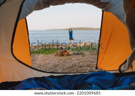 view from a tent on the shore of a lake or sea, a woman collects firewood or does yoga and meditation. camping in nature, wild life in a tent. freedom and relaxation from the hustle and bustle of the