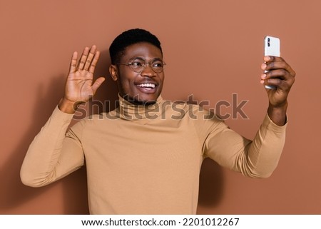 Portrait of handsome trendy cheerful guy blogger taking selfie waving greetings isolated over brown color background