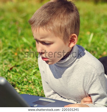 Toned photo of Serious Kid with Laptop on the Grass
