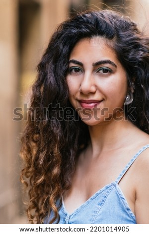 vertical portrait of an attractive arabic woman dressing denim dress and looking at camera in the street Royalty-Free Stock Photo #2201014905