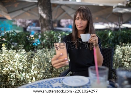 Morning in cafe - attractive woman in black drinkin coffe and make selfie photo for social networks. stock photo