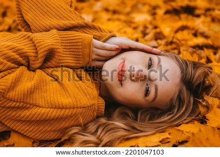 Beautiful girl lies in autumn leaves in the park, autumn. Young girl with perfect skin in a yellow sweater looks at the camera Royalty-Free Stock Photo #2201047103