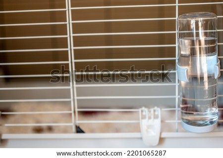Selective focus on a water bottle mounted on the bars of a small animal cage. 