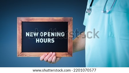New Opening Hours. Doctor shows sign board with wooden frame. Background blue