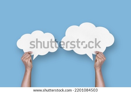 hand holding white paper cloud shape speech bubble balloon isolated on light blue background communication bubbles
