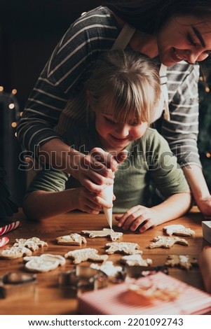 Christmas, New Year gingerbread cooking, making, decorating freshly baked cookies with icing and mastic. Mommy and child, authentic lovely moments. Mom helping cute little daughter to decorate cookie