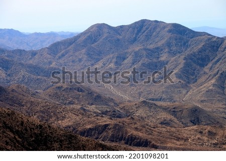 Aerial picture of Joshua Tree national park mountain range with blue skies. Impressive mountain range with single tree hiking trail in the valley. Drone image of Californian nature landscape.