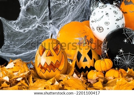 Halloween's holiday attributes. Lantern carved from pumpkin known as Jack-o-lantern on a black background with spider webs, autumn leaves and balloons. Trick or treat.