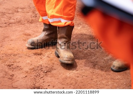 A construction worker is fully wear PPE such as safety shoe and coverall unitform is standing on dirt ground. Industrial worker and equipment object photo. Selective focus.