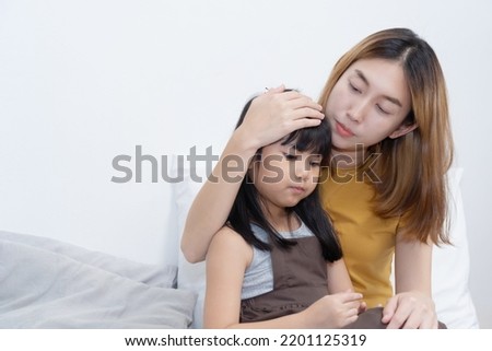 Asian Caring Mother holding her sick daughter and measuring temperature with her hand.  Royalty-Free Stock Photo #2201125319