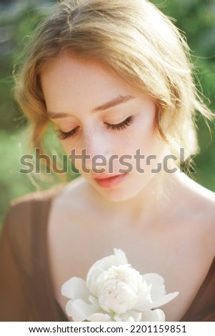 Close-up portrait of a cute blonde with a white flower in her hand. Soft blur background