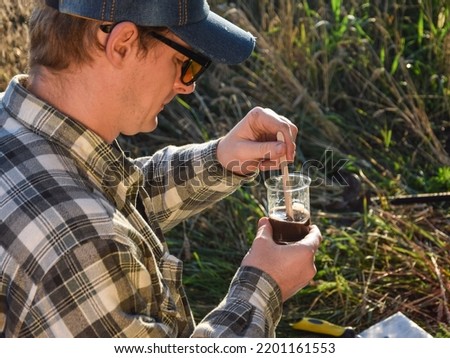 Male agronomy specialist testing soil sample outdoors, using laboratory equipment, performing soil certification at agricultural grain field sunrise. Environment research, soil certification