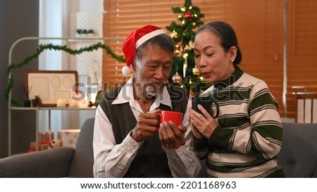 Happy senior couple sitting on couch next to a decorated Christmas tree and enjoying drinking hot chocolate together