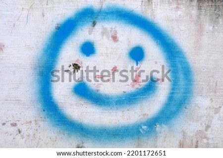 Image or illustration of a blue smile icon made using spray paint on the wall
