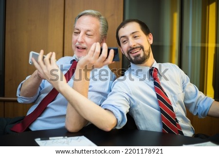Two smiling colleagues taking selfie in his office
